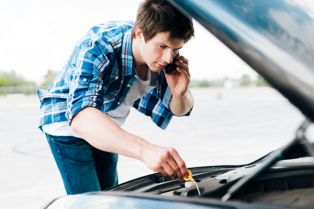 A young person calling roadside assistance service to recover his car from drained battery.